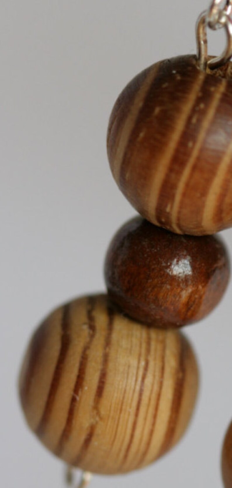 May include: A close-up of a wooden bead necklace with brown and light brown striped beads. The beads are round and have a smooth finish.