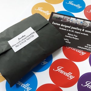 May include: A gray paper package with a white label that says "Jewellsy etsy.com/shop/Jewellsy Mel 07818 422722". The package is sitting on a white surface with several round stickers that say "Jewellsy" in different colors.
