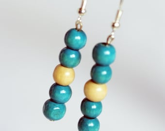 May include: A pair of dangle earrings with blue and beige wooden beads. The earrings are silver and have a simple hook closure.