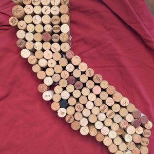 May include: A collection of wine corks arranged in the shape of California, with various markings and dates visible. The corks are primarily light brown with some darker and lighter variations, set against a red background.