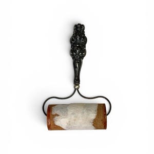 May include: A lint roller featuring a dark, ornate metal handle with intricate scrollwork and a cylindrical adhesive roller head covered in white lint-collecting paper. The metal frame connects the decorative handle to the rotating roller.