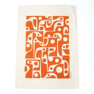 Op de afbeelding: Een witte keukendoek met een oranje abstract geometrisch patroon. De tekst "The Modern Folk" is afgedrukt in de rechterbenedenhoek.