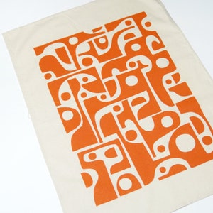 Op de afbeelding: Een witte tote bag met een oranje abstract geometrisch ontwerp. Het ontwerp bestaat uit verschillende vormen en krommen.