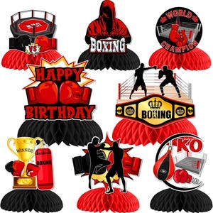 May include: A collection of boxing-themed party decorations. Includes red and black honeycomb centerpieces with boxing gloves, a ring, a trophy, and the words "Happy Birthday" and "World Champion".