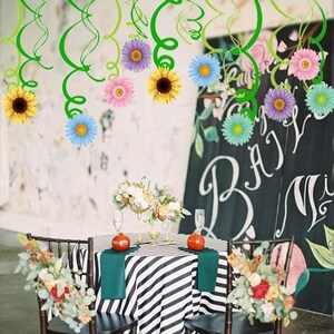 May include: A decorated table setting for a wedding or event. The table has a black and white striped tablecloth, green napkins, and floral arrangements. Hanging from above are green streamers and colorful paper flowers.
