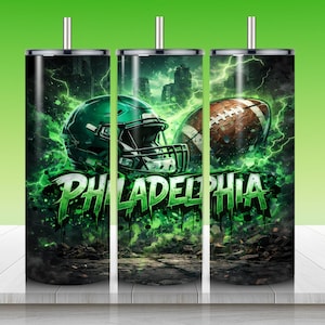 Puede incluir: Un vaso de acero inoxidable con un dise&ntilde;o que presenta un casco de f&uacute;tbol americano verde y un bal&oacute;n de f&uacute;tbol marr&oacute;n. El fondo muestra un horizonte de la ciudad y rel&aacute;mpagos verdes. La palabra "PHILADELPHIA" est&aacute; en verde, con letras goteando.