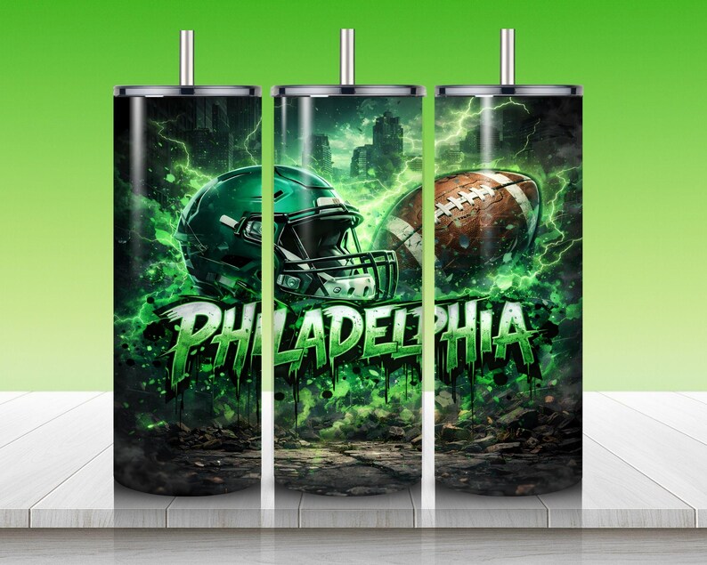 Puede incluir: Un vaso de acero inoxidable con un dise&ntilde;o que presenta un casco de f&uacute;tbol americano verde y un bal&oacute;n de f&uacute;tbol marr&oacute;n. El fondo muestra un horizonte de la ciudad y rel&aacute;mpagos verdes. La palabra "PHILADELPHIA" est&aacute; en verde, con letras goteando.