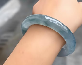 May include: A translucent, pale blue-green jadeite bangle bracelet. The smooth, polished surface reflects light, showcasing the natural variations in color. The bracelet is a solid, circular design, perfect for everyday wear.