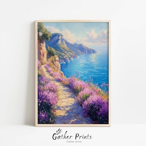 May include: A framed print of a coastal landscape. A stone path winds along a cliff, lined with purple flowers, overlooking a turquoise sea. Mountains and a town are visible in the distance under a blue sky with clouds. The print is in a light wood frame.