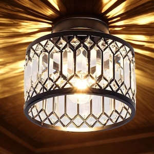 Puede incluir: Una lámpara de techo cilíndrica negra con un diseño geométrico. La lámpara presenta detalles de cristal transparente facetado y una fuente de luz brillante. La luz proyecta un brillo cálido y sombras intrincadas.