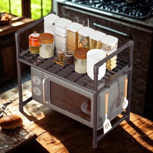 May include: A gray microwave oven with a dark gray metal rack on top, holding various glass jars and containers. The rack also has hanging kitchen utensils. The microwave is on a wooden surface, with a kitchen in the background.