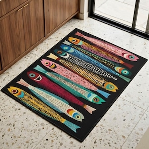 May include: A rectangular black rug featuring a colorful pattern of stylized fish. The fish are in various colors, including yellow, blue, pink, and green, with detailed scales and eye designs. The rug is placed on a tiled floor.
