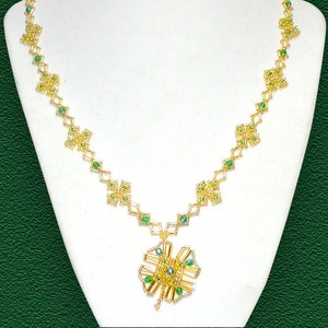 Puede incluir: Un collar de oro con un colgante verde y dorado en forma de trébol de cuatro hojas. El collar está hecho de pequeñas cuentas y está enhebrado en una cadena delicada.