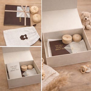 May include: A gift set for a baby, including a box, a book titled "THE FIRST STORY ABOUT YOU", two small wooden boxes, a muslin bag, and a teddy bear. The box is white, and the book is brown with a ribbon.