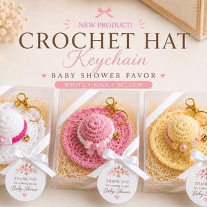 May include: Three crochet hat keychains in clear boxes, perfect for a baby shower. The hats are white, pink, and yellow, each with a matching bow and gold keychain. Each box has a tag that says "THANK YOU for coming to my Baby Shower."