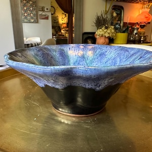 May include: A ceramic bowl with a scalloped rim featuring a glossy blue and purple mottled glaze on the interior and upper exterior, transitioning into a solid black base. The bowl has a wide, open shape with a smooth, curved silhouette.