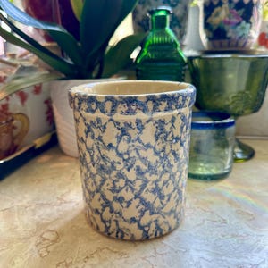 May include: A cylindrical stoneware pot with a cream-colored base and a blue, mottled pattern. The rim is also blue. The pot is likely for kitchen or home decor.