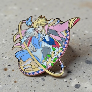 May include: Enamel pin depicting a romantic scene with two figures in a loving embrace. The pin has a gold outline and a pink, blue, and white colour scheme. The design includes floral elements and a stylized background.