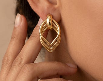 May include: A gold-toned earring featuring a multi-layered, geometric drop design. The earring consists of three interconnected, smooth, polished metal loops that form a pointed, elongated shape, suspended from a single rounded top connector.
