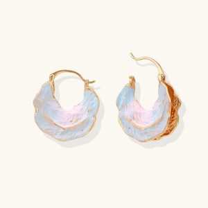 May include: A pair of gold-tone hoop earrings with a layered, petal-like design. The earrings feature a light blue and pink color scheme with gold accents. The earrings are designed to be worn on the ear.