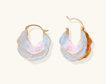 May include: A pair of gold-tone hoop earrings with a layered, petal-like design. The earrings feature a light blue and pink color scheme with gold accents. The earrings are designed to be worn on the ear.