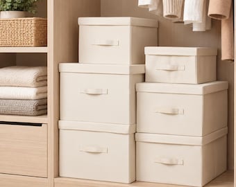 May include: A set of five rectangular off-white fabric storage boxes with lids and integrated handles, stacked in a wooden closet. The boxes feature a clean, solid-colored textile exterior and are arranged in two columns of varying sizes.