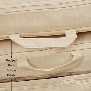 May include: A stack of rectangular cushions made from undyed pure cotton fabric. Each cushion features a matching fabric handle attached to the side and a horizontal zipper closure. The text Undyed Pure Cotton Fabric is printed on the side.