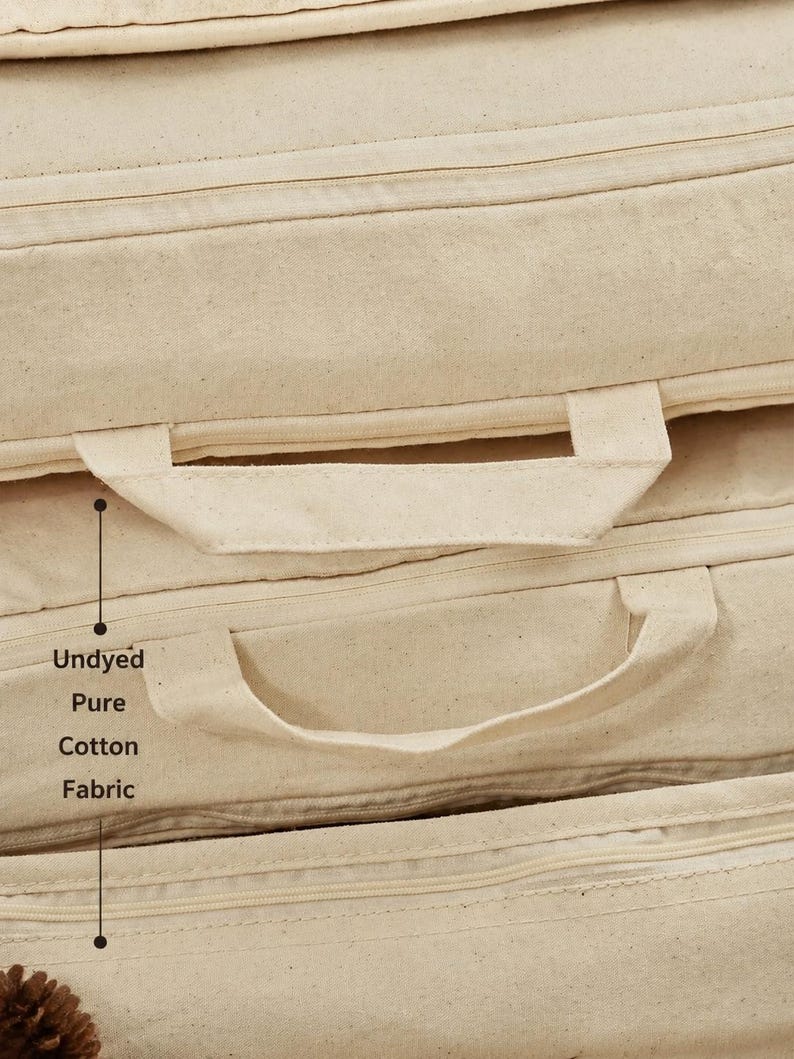 May include: A stack of rectangular cushions made from undyed pure cotton fabric. Each cushion features a matching fabric handle attached to the side and a horizontal zipper closure. The text Undyed Pure Cotton Fabric is printed on the side.