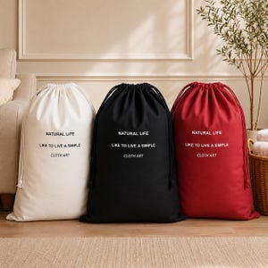 Pode incluir: Três sacos com cordão nas cores branca, preta e vermelha. Cada saco apresenta o texto impresso NATURAL LIFE, LIKE TO LIVE A SIMPLE e CLOTH ART numa fonte centrada. Os sacos possuem cordões a condizer no topo para fecho e armazenamento.