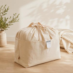 May include: A large, off-white canvas storage bag with a drawstring closure and two top handles. The bag features a rectangular front pocket with a small white label attached that reads "TOUR-MABOU" with blank lines below for writing information.