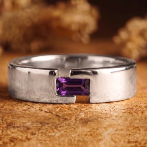 May include: A silver-toned metal ring featuring a tension-set, rectangular, deep purple amethyst gemstone. The band has a smooth, polished finish with a distinct gap where the stone is securely held between the two ends of the metal band.