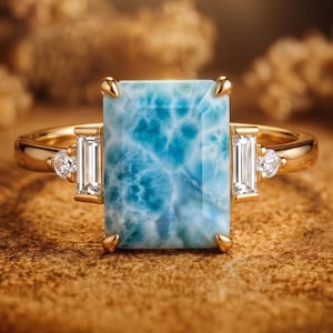 May include: A gold ring featuring a large, rectangular, marbled blue Larimar gemstone at the center, flanked by two vertical baguette-cut diamonds and two smaller round-cut diamonds set into the polished gold band on each side.