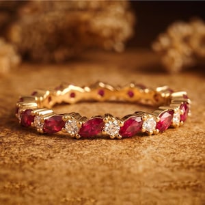 May include: A gold eternity band featuring an alternating pattern of marquise-cut red rubies and round-cut clear white diamonds. The ring is crafted with a continuous metal setting that holds each gemstone securely in place around the entire band.