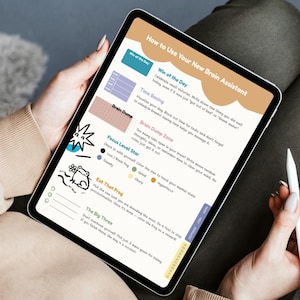 May include: A digital tablet showing a productivity planner titled "How to Use Your New Brain Assistant." The planner includes sections for daily wins, time boxing, and a "Brain Dump Zone." A white stylus is held in the hand.