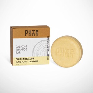 May include: A light brown cardboard box and a round, light yellow shampoo bar. The box reads "pure spruce" and "Calming Shampoo Bar, Golden Meadow, Ylang Ylang + Cedarwood." The bar is stamped with "pure spruce." For dry/sensitive hair.