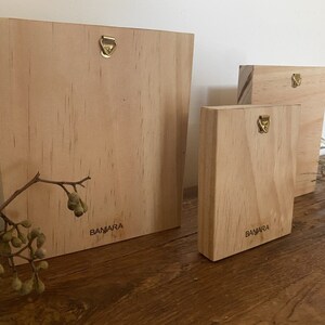 May include: Three wooden plaques with a brass hanging hook. The plaques are all natural wood and have the word "BAMARA" printed on them.