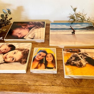 May include: Five wooden photo blocks with different images printed on them. The images include a baby sleeping, two children, a woman and a girl, a person doing a handstand on a beach, and a dog.