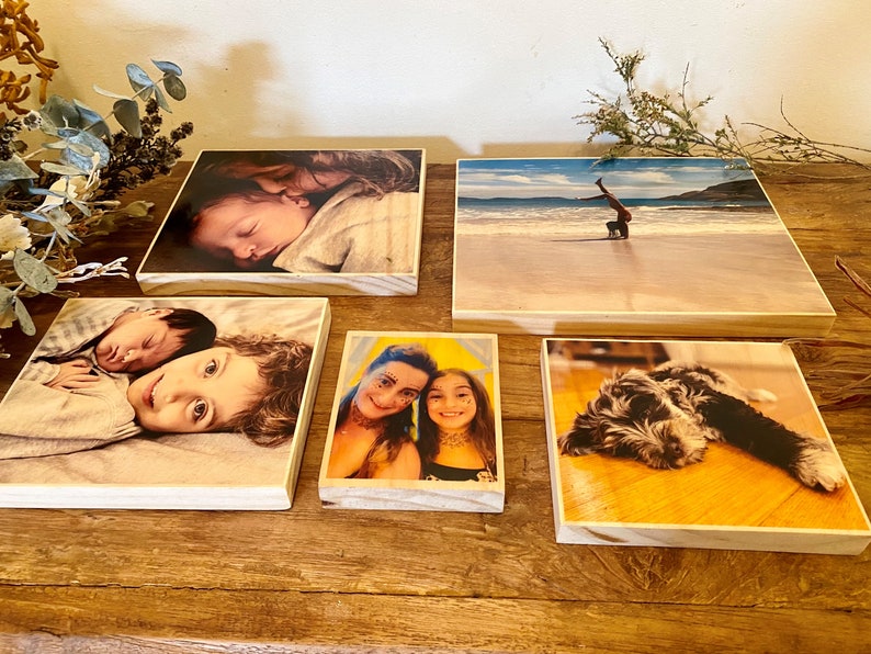 May include: Five wooden photo blocks with different images printed on them. The images include a baby sleeping, two children, a woman and a girl, a person doing a handstand on a beach, and a dog.