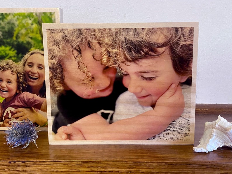 May include: A wooden photo block with a printed image of two children hugging. The children have curly hair and are smiling. The photo block is a light brown color.
