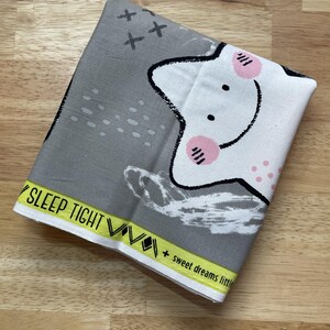 May include: Folded gray and white fabric with a cartoon star design. The star has pink cheeks and black outlines. The fabric has the text "SLEEP TIGHT" and "+ sweet dreams little" in yellow.