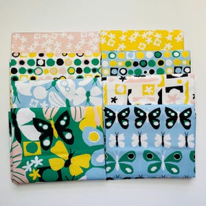 May include: A collection of folded fabric squares with various colorful patterns. Designs include floral, geometric shapes, and butterfly motifs in shades of pink, yellow, green, and blue. The fabrics are neatly stacked, showcasing the diverse patterns.