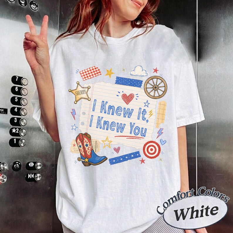 May include: A white t-shirt featuring a central graphic of a lined notepad page with the blue text I Knew It, I Knew You. The design includes a red heart, a brown cowboy boot, a sheriff star, a wagon wheel, and various small colorful shapes.