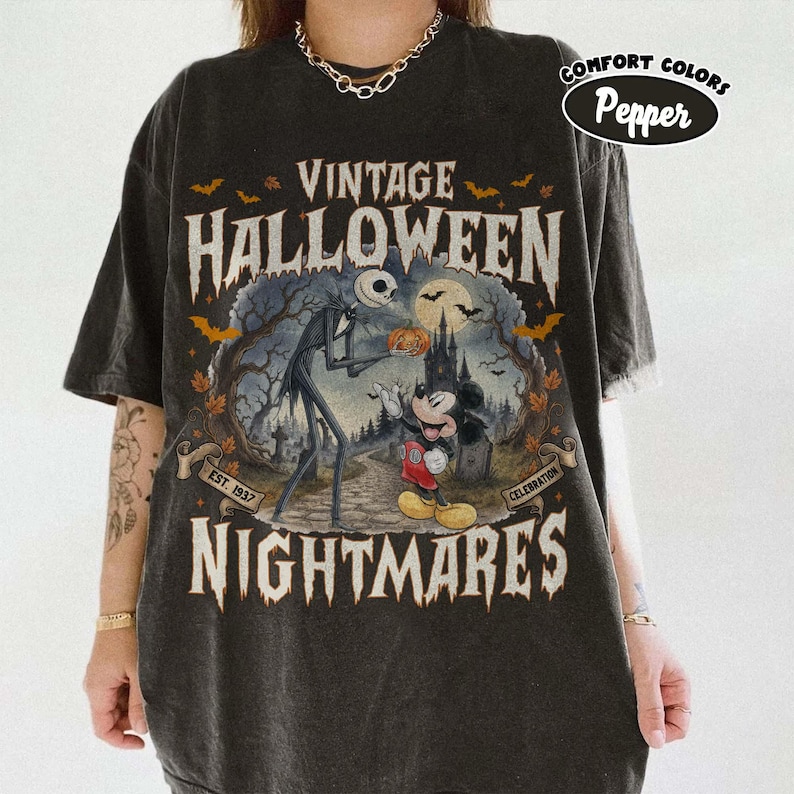 Puede incluir: Una camiseta gris carb&oacute;n con un estampado gr&aacute;fico que incluye el texto VINTAGE HALLOWEEN NIGHTMARES. El dise&ntilde;o muestra a Jack Skellington y Mickey Mouse en un paisaje espeluznante con un castillo, murci&eacute;lagos y una calabaza, incluyendo el texto EST. 1937.