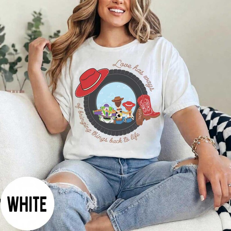 Pu&ograve; includere: Una t-shirt bianca con una grafica raffigurante uno pneumatico nero che incornicia personaggi dei cartoni animati, un cappello da cowboy rosso e uno stivale da cowboy rosso. Il testo Love has ways of bringing things back to life circonda l'immagine.