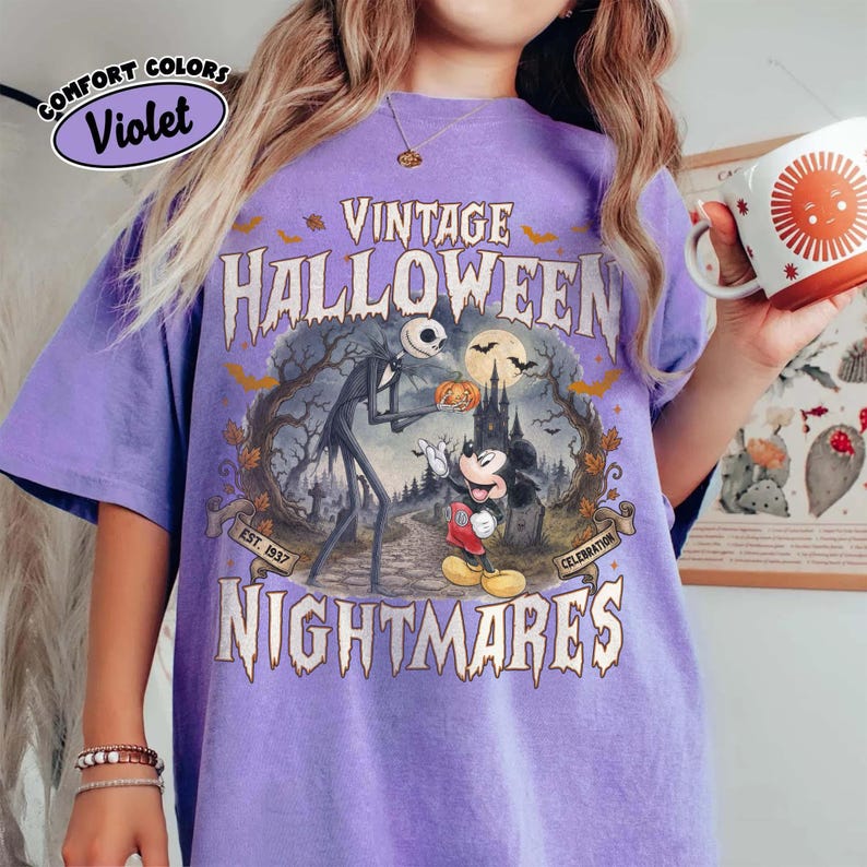 Puede incluir: Una camiseta violeta con un estampado gr&aacute;fico con el texto VINTAGE HALLOWEEN NIGHTMARES. El dise&ntilde;o muestra una figura esquel&eacute;tica alta y un rat&oacute;n de dibujos animados en un cementerio con luna llena, murci&eacute;lagos y &aacute;rboles. Una peque&ntilde;a etiqueta dice COMFORT COLORS Violet.