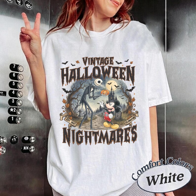 Puede incluir: Una camiseta blanca de manga corta con un estampado gr&aacute;fico que incluye el texto VINTAGE HALLOWEEN NIGHTMARES EST. 1937 CELEBRATION. La ilustraci&oacute;n muestra a Jack Skellington y Mickey Mouse en un bosque tenebroso con murci&eacute;lagos y un castillo.