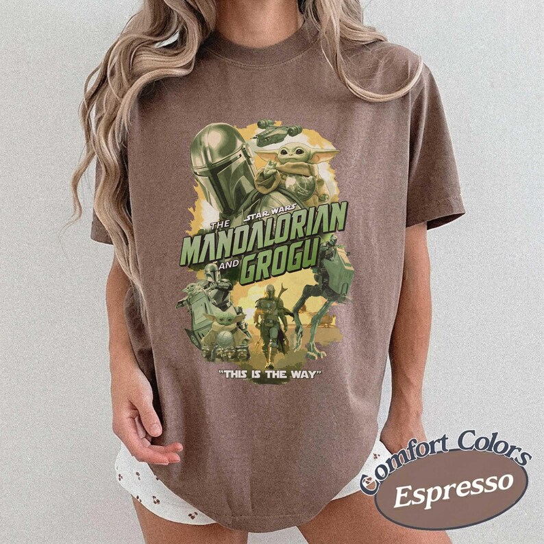May include: Espresso-colored t-shirt featuring a graphic from The Mandalorian series. The design includes the text "The Mandalorian and Grogu" and "This is the Way." The shirt has a relaxed fit and is made of a soft material.