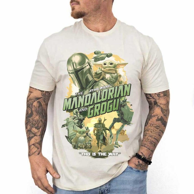 May include: Cream-colored t-shirt featuring a graphic from the Star Wars series, "The Mandalorian and Grogu." The design includes images of the Mandalorian, Grogu, and other characters, with the phrase "This is the Way."