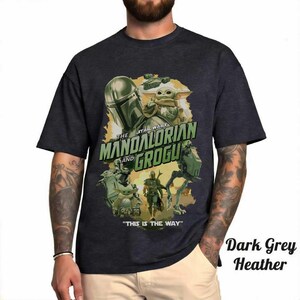 May include: Dark grey heather t-shirt featuring a graphic of The Mandalorian and Grogu from Star Wars. The design includes the text "THE MANDALORIAN and GROGU" and "THIS IS THE WAY". The shirt has a crew neck and short sleeves.