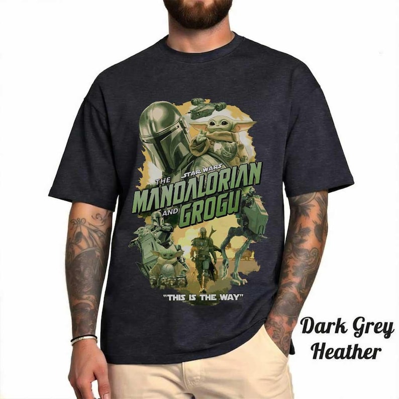May include: Dark grey heather t-shirt featuring a graphic of The Mandalorian and Grogu from Star Wars. The design includes the text "THE MANDALORIAN and GROGU" and "THIS IS THE WAY". The shirt has a crew neck and short sleeves.